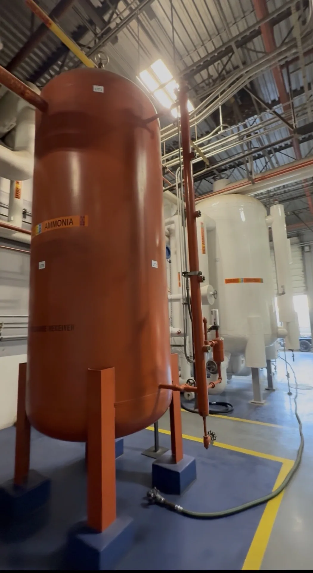 Orange ammonia pressure receiver vessel inside an industrial refrigeration machine room